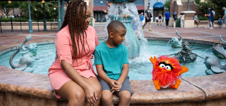A woman and a child sitting in front of a fountain at Walt Disney World with a stuffed animal.