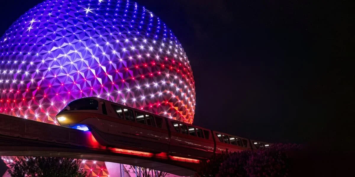 The Disney Monorail passes near Spaceship Earth at EPCOT with an American flag nearby